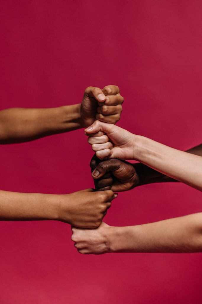 Close-up of diverse hands forming fists, symbolizing unity and teamwork on a vivid pink background.